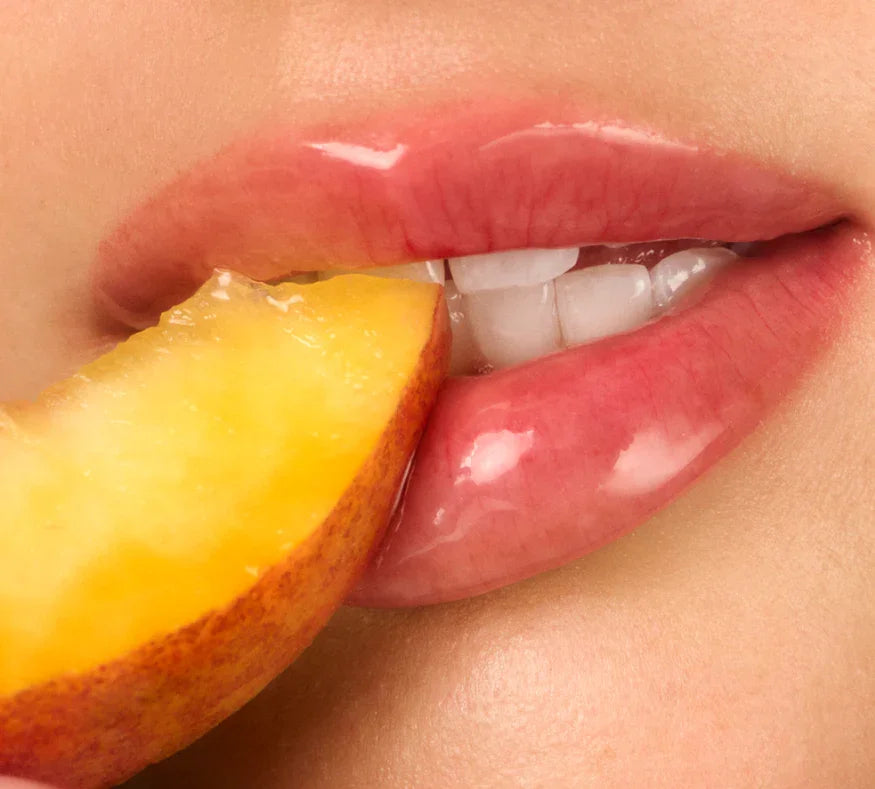 Close-up of a person biting into a peach slice with a focus on the lips and peach.